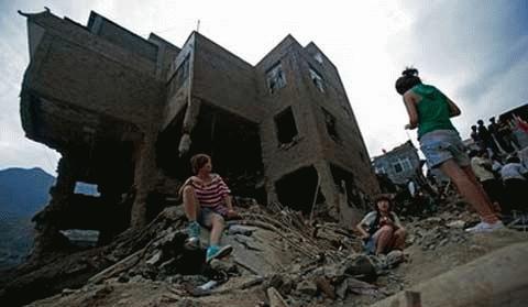 Người dân Trung Quốc ngồi cạnh một tòa nhà bị động đất phá hủy ở Zhouqu, tỉnh Gansu, để chờ tin tức người thân mất tích. (Ảnh: AP)